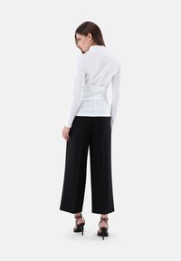 Camicia bianca aderente con colletto a punta, vita aderente e maniche lunghe, abbinata a pantaloni neri a gamba larga e tacchi alti neri con cinturini.