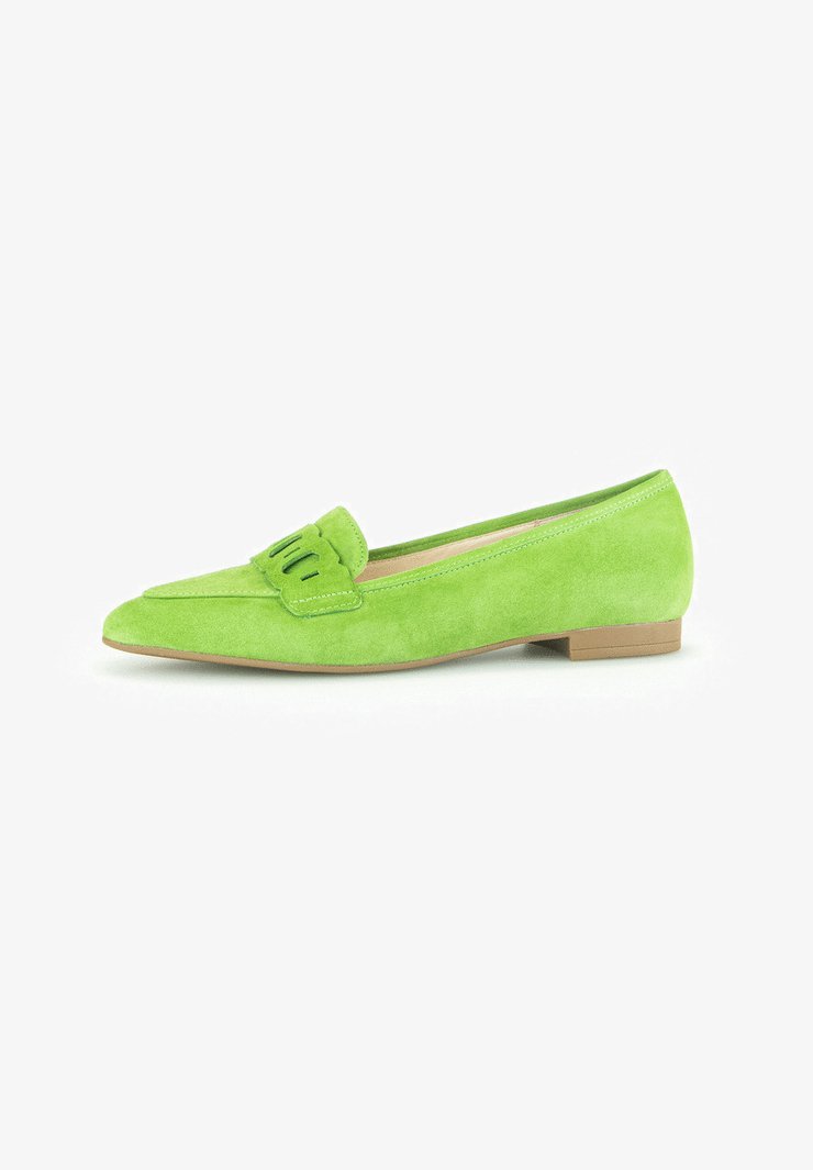 Chaussure plate en suède vert avec un bout pointu et un détail décoratif en pompon. La semelle est marron clair et la texture est douce et lisse.