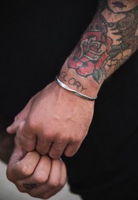 Metāla aproce uz rokas, iegravēta ar vārdu "GLORY", apkārties kcolourful roze tetovējums. Izteiksmīga teksturēta apdare un eleganta, izliektā forma.