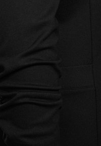 Černá mikina s měkkou, strukturovanou tkaninou. Má hladký siluetu a nařasené manžety. Obsahuje detail postranní kapsy.