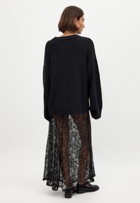 Overdimensioneret sort strikket sweater med ribbet kant, lagdelt over en gennemsigtig brun blonde-nederdel med blomsterprint, båret med sorte sko.