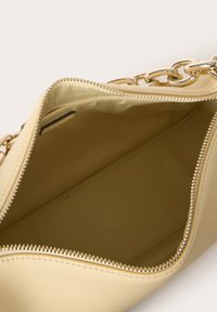 Borsa in pelle gialla con apertura con zip. L'interno presenta una texture liscia e ampio spazio. Accento in catena con hardware dorato visibile.
