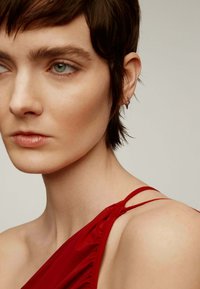 Vestido rojo de un solo hombro con detalles fruncidos, que muestra una tela suave y una silueta ajustada, acompañado de un simple accesorio de cuff en la oreja.