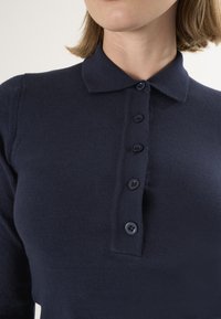 Granatowy dzianinowy polo z klasycznym kołnierzykiem, sześcioma guzikami na listwie oraz ściągaczowymi mankietami, o gładkiej fakturze i dopasowanym kroju.