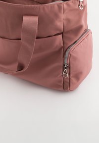 Roze nylon draagtas met een gestructureerde oppervlakte, voorzien van een groot hoofdcompartiment, een buitenzipvak en stevige stoffen handvatten.