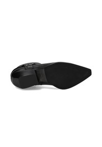 Suela de zapato de cuero negro con forma puntiaguda, tacón plano y textura suave. Presenta tachuelas metálicas y un logotipo en relieve en la superficie.