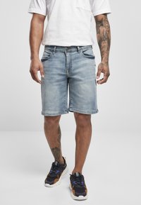 Denim shorts i lyseblå med en falmet finish, fem lommer og lige pasform. Båret med sorte og orange træningssko.
