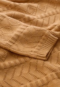 Sweter w musztardowym kolorze z oplotem, charakteryzujący się teksturowanym wzorem w zygzak i ściągaczami przy mankietach dla dodatkowego efektu. Miękka i ciepła tkanina.