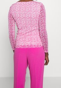 Långärmad topp med ett mönster i rosa och vitt, matchad med klara rosa byxor. Båda plaggen har en slät textur.