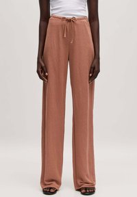 Wijdvallende broek in een zachte roze stof, met een elastische tailleband en een trekkoord. Een gladde textuur met een ontspannende pasvorm en een volledig lengte ontwerp.