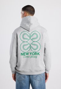 Felpa grigia con una grande grafica verde e testo sulla schiena, che mostra "NEW YORK Tennis Society." Presenta un cappuccio con cordoncino e polsini a coste.