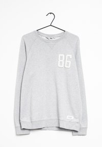 Sweat-shirt gris avec manches raglan, arborant un "86" blanc texturé sur le devant et une étiquette sur l'ourlet inférieur. Matière en mélange de coton doux.