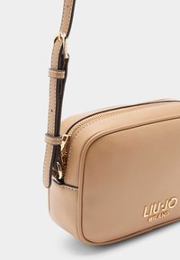 Karamelli nahkine ristiõla kott kuldsete detailidega, lukuga sulgemine ja tekstureeritud pind. Omab kontrastset tumedat rihma koos õmbluse detailidega.