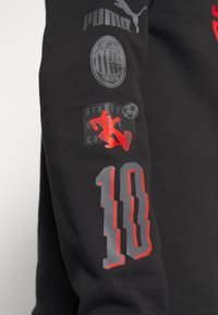 Sort sweatshirt med Puma- og AC Milan-logoer, med røde og grå grafikere, inklusive "Street Soccer Cup" og nummer "10" på ærmet.