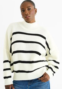 Maglione lavorato a maglia con collo alto, base bianca con audaci strisce nere, vestibilità rilassata e polsini a costine. Completa un abbigliamento casual.