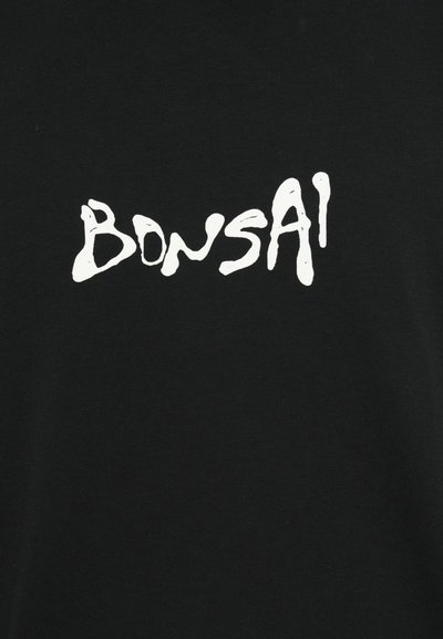 Melna T-kreklu ar drosu baltu uzrakstu "BONSAI" rotaļīgā, noplūstošā fontā. Gluda auduma tekstūra ar klasisku apaļu kakla dizainu.