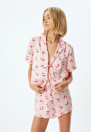 Rosa kurzes Pyjama-Set mit Kirschmotiv, bestehend aus einem kurzärmligen Oberteil, einer typischen Krawattenfront und Shorts mit Kordelzug, gefertigt aus leichtem Stoff.