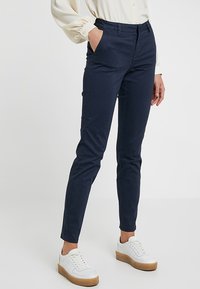 Granatowe, slim-fit spodnie wykonane z mieszanki bawełny, z bocznymi kieszeniami i gładkim wykończeniem, zestawione z białymi trampkami.