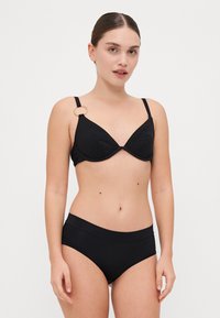 Juodas bikini rinkinys, turintis tekstūruotą, raštuotą liemenėlę su V formos puodeliu ir apvaliu auksiniu akcentu ant vienos petnešėlės, derinamas su atitinkančiomis aukšto juosmens kelnaitėmis.