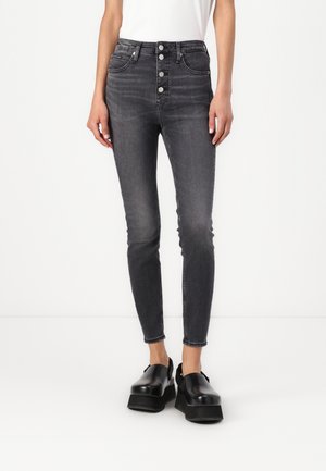 Jeans gris de cintura alta con un ajuste slim, cierre de cinco botones y un ligero desteñido, combinados con zapatos de plataforma negros y gruesos.