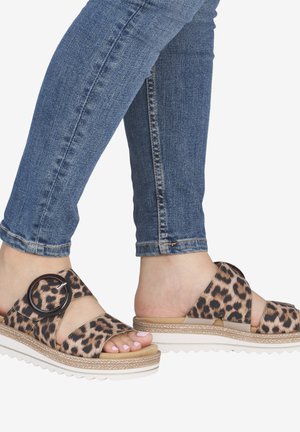 Pies con vaqueros pitillo azules y sandalias con estampado de leopardo, hebilla grande negra y suelas de plataforma blancas.