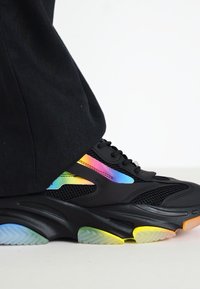 Black sneakers with a chunky sole, featuring iridescent accents in rainbow colors and mesh detailing for breathability.