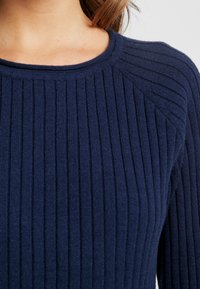 Mörkblå ribbad tröja med rundad hals och texturerad design. Har vertikala ränder och raglanärmar för en figurnära passform.