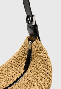 Szövetelt készült világosbarna táska, érdes felülettel, fekete bőr pánttal és ezüst cipzárral, amelyhez textil húzózsinór tartozik.