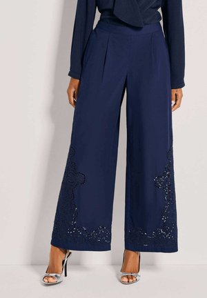 Marineblauwe wijde broek met ingewikkeld kantdetail en pailletten aan de zoom. Gemaakt van zachte stof met een gladde textuur en een plooivorm aan de voorkant.