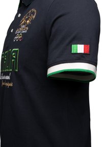 Polo di colore blu navy con colletto verde smeraldo. Presenta un patch ricamato della bandiera italiana sulla manica e dettagli con logo sul fronte.