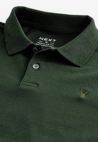 Polo de color verde oscuro hecho de tejido texturizado, con cuello, dos botones y un pequeño logo bordado en el pecho.