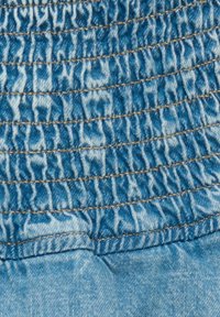 Denimtyg i blått med smockad struktur, med en samlad design och kontrasterande bruna sömmar längs sömmarna.