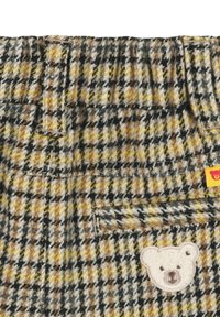 Wollen stoffenmix in een geel, zwart en bruin houndstooth patroon met een berenpatch en pocketdetail aan de rechterkant.