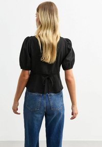 Zwart top met pofmouwen en een aansluitende taille, met een strikdetail op de rug, gecombineerd met hooggesneden blauwe spijkerbroek. Soepele textuur.