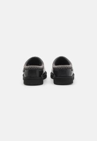 Fekete slip-on cipők, texturált bőrből, kontrasztos varrással ellátott szegéllyel és alacsony profilmagasságú gumitalppal.