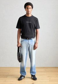 Black cotton t-shirt with white logo, light blue jeans with a gradient effect, black belt, black bag, and black sneakers with white stripes.