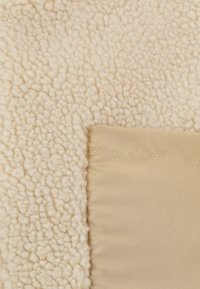 Tissu en polaire de couleur crème avec une surface douce et texturée, associé à un panneau beige lisse cousu sur le côté.