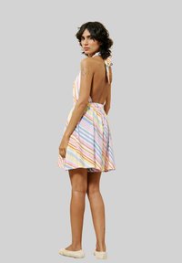 Gestreiftes Kleid in Pastellfarben. Mit Halterneck-Design, offener Rückseite und elastischem Bund. Das Modell trägt hellfarbige Schuhe.