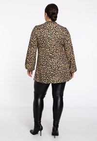 Leopardenmuster-Oberteil mit langen Puffärmeln, beigem und schwarzem Muster, kombiniert mit glänzenden schwarzen Lederleggings und schwarzen Absatzstiefeln.
