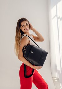 Schwarzer Leder-Rucksack mit silbernem Zubehör, rechteckiger Form, Obergriff und verstellbaren Riemen. Besitzt ein Logo-Patch auf der Vorderseite.