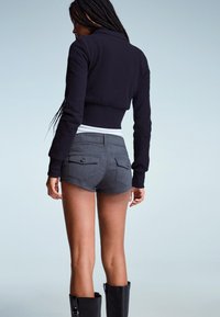 Felpa nera corta con colletto, abbinata a pantaloni corti grigi con due tasche posteriori e dettagli in bottone neri. Design semplice e aderente.