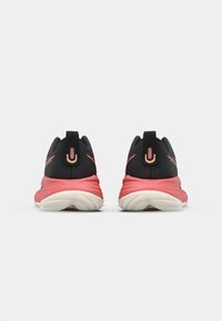 Chaussures de sport noires et roses, avec une tige en textile, un talon arrondi et une semelle striée. Des accents notables incluent un petit logo et des coutures contrastées.