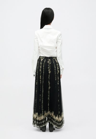 Duga crna suknja s cvjetnim uzorkom u krem i zlatnoj boji, uparena s pripijenom bijelom košuljom, prikazana s leđa s naboranom teksturom.