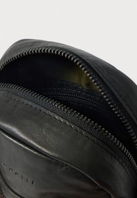 Interior de bolsa de couro preto com compartimentos duplos com fecho de correr e textura suave. Apresenta ferragens metálicas nos fechos de correr e um logótipo subtil em relevo.