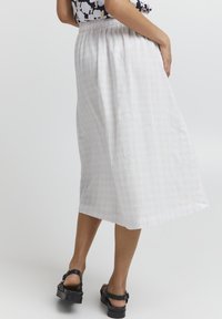 Hvid midi-skjørt med ternet mønster, elastisk talje og en flydende design. Sammen med sorte plateau-sandaler.