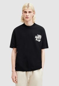 Tricou din bumbac negru cu mâneci scurte, având o grafică albă pe partea stângă a pieptului. Se potrivește lejer, cu un gât rotund.