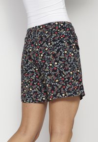 Pantaloni corti neri con motivo floreale e cintura elastica, con piccoli dettagli rossi, gialli e verdi su uno sfondo scuro.