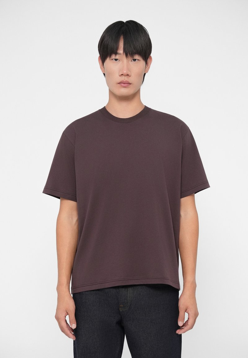 Donkerbruine t-shirt met korte mouwen en ronde halslijn, met een losse fit, gemaakt van zachte stof, gecombineerd met donkere spijkerbroeken.