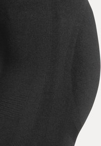 Svarta leggings med en slät, texturerad yta och en figurnära passform. Tyget verkar stretchigt och andningsbart, utan mönster.