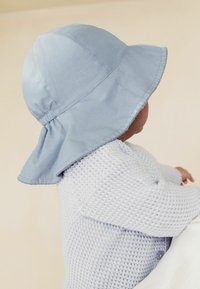 Lichtblauwe katoenen bucket hat met een brede rand en een verzamelde naad aan de kroon, gecombineerd met een gestructureerde lichtblauwe trui.